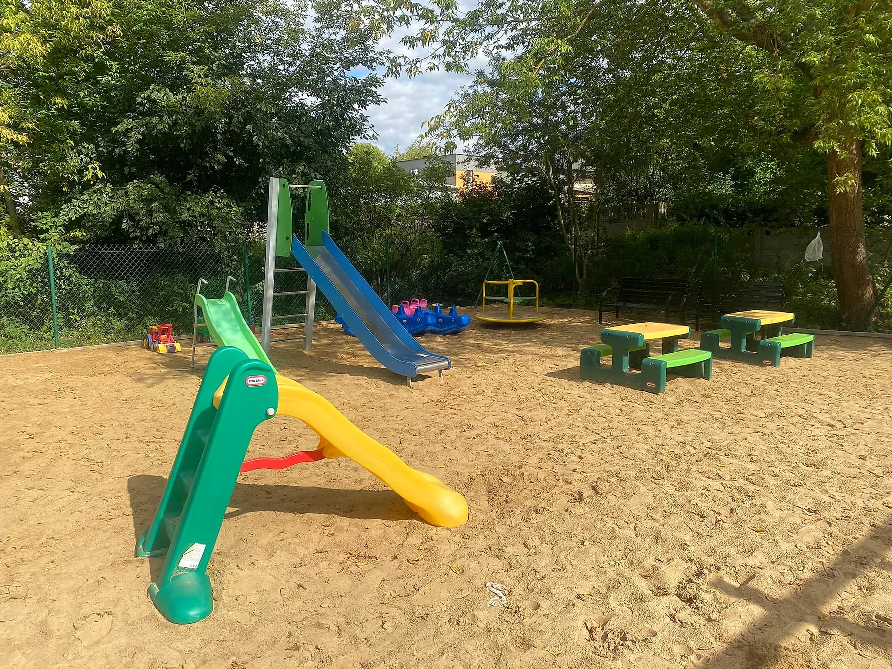 Plac zabaw z małą zjeżdżalnią i stolikami w cieniu drzew
