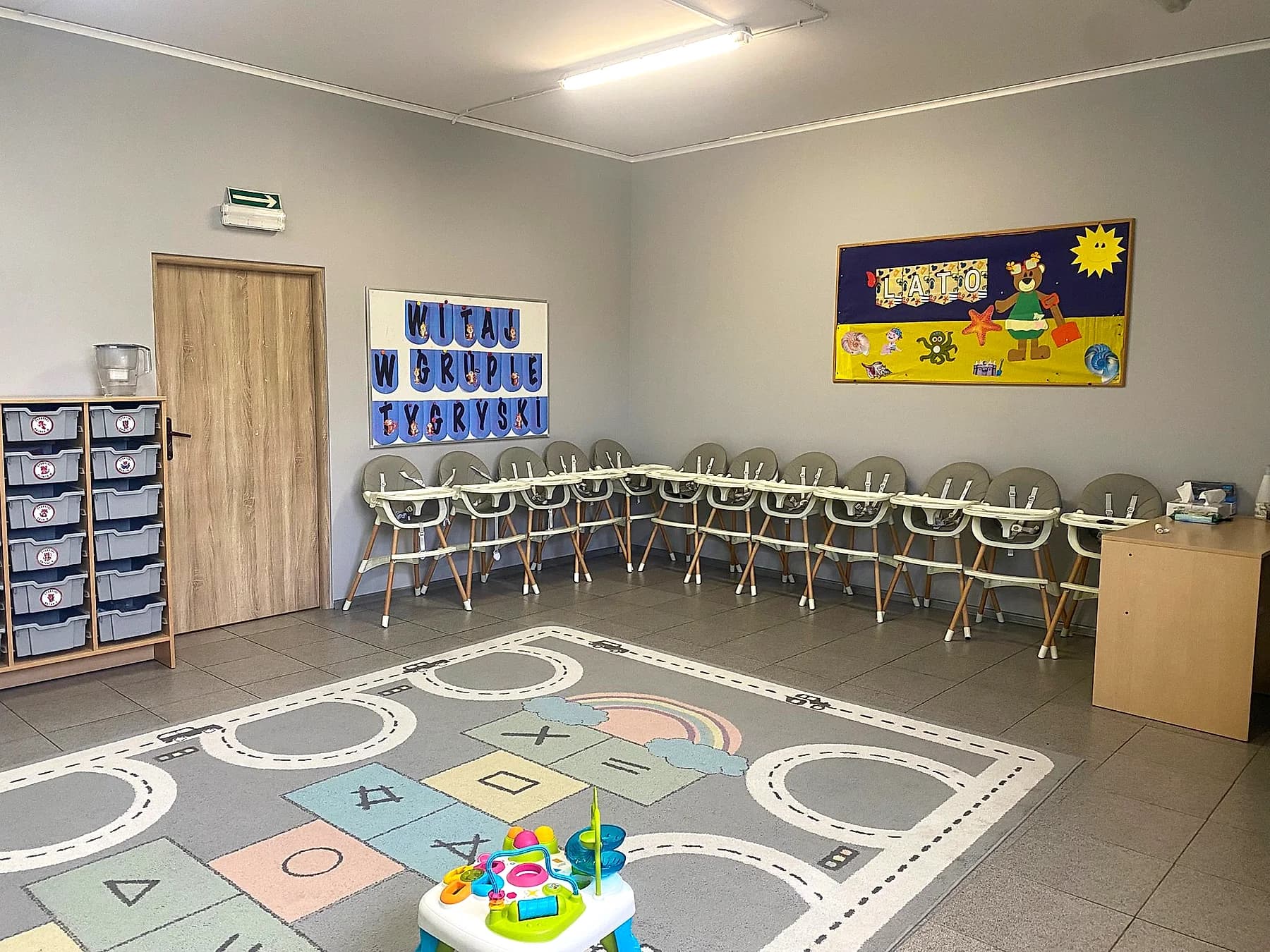Sala z dywanem w kształty, tablicą powitalną i krzesełkami