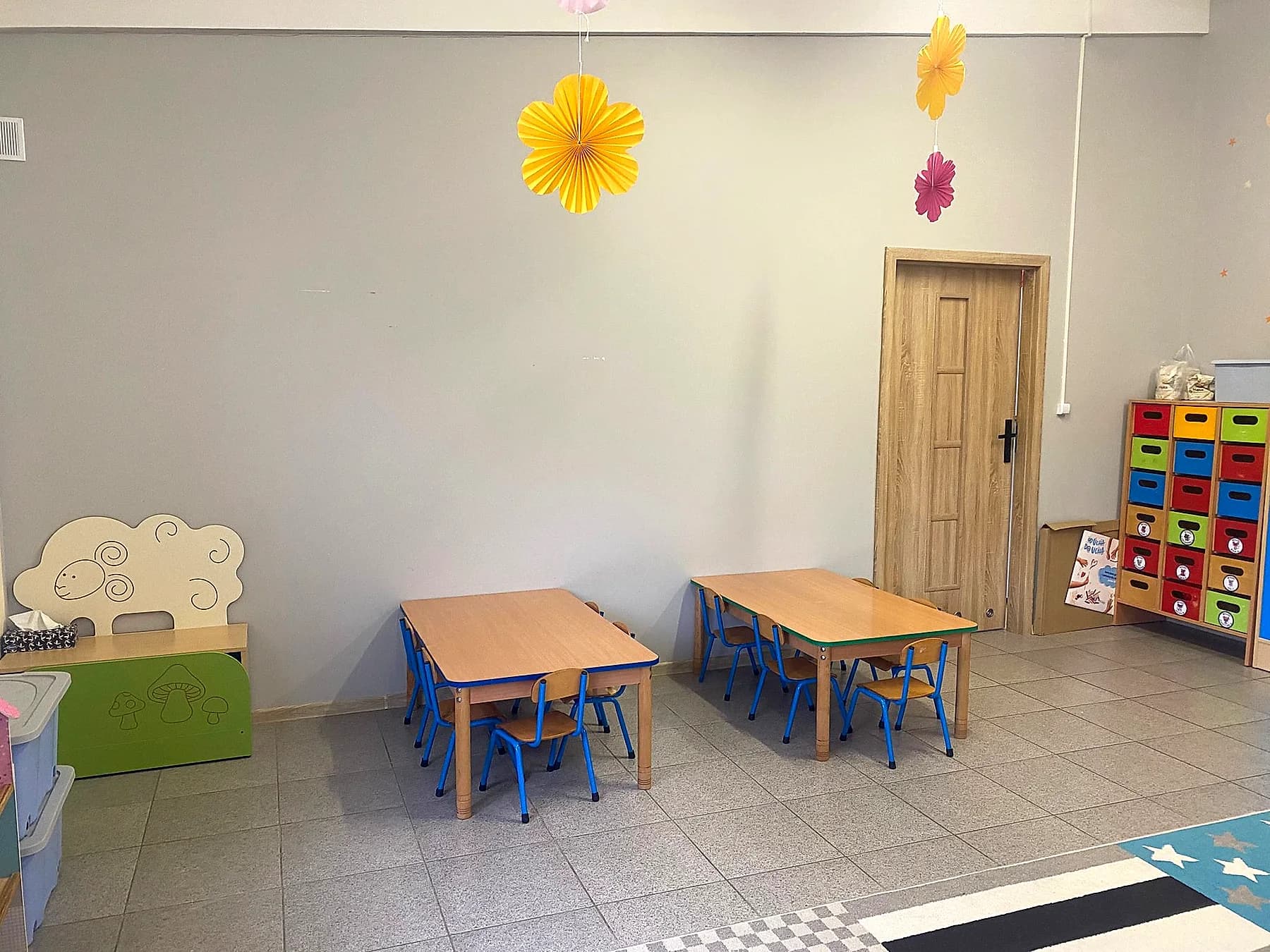 Stoliki do zajęć i kącik z pojemnikami na zabawki
