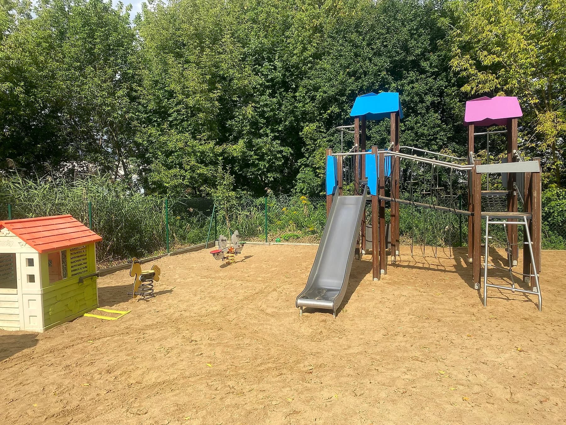 Wieża ze zjeżdżalnią i domek do zabawy wśród zieleni na placu zabaw